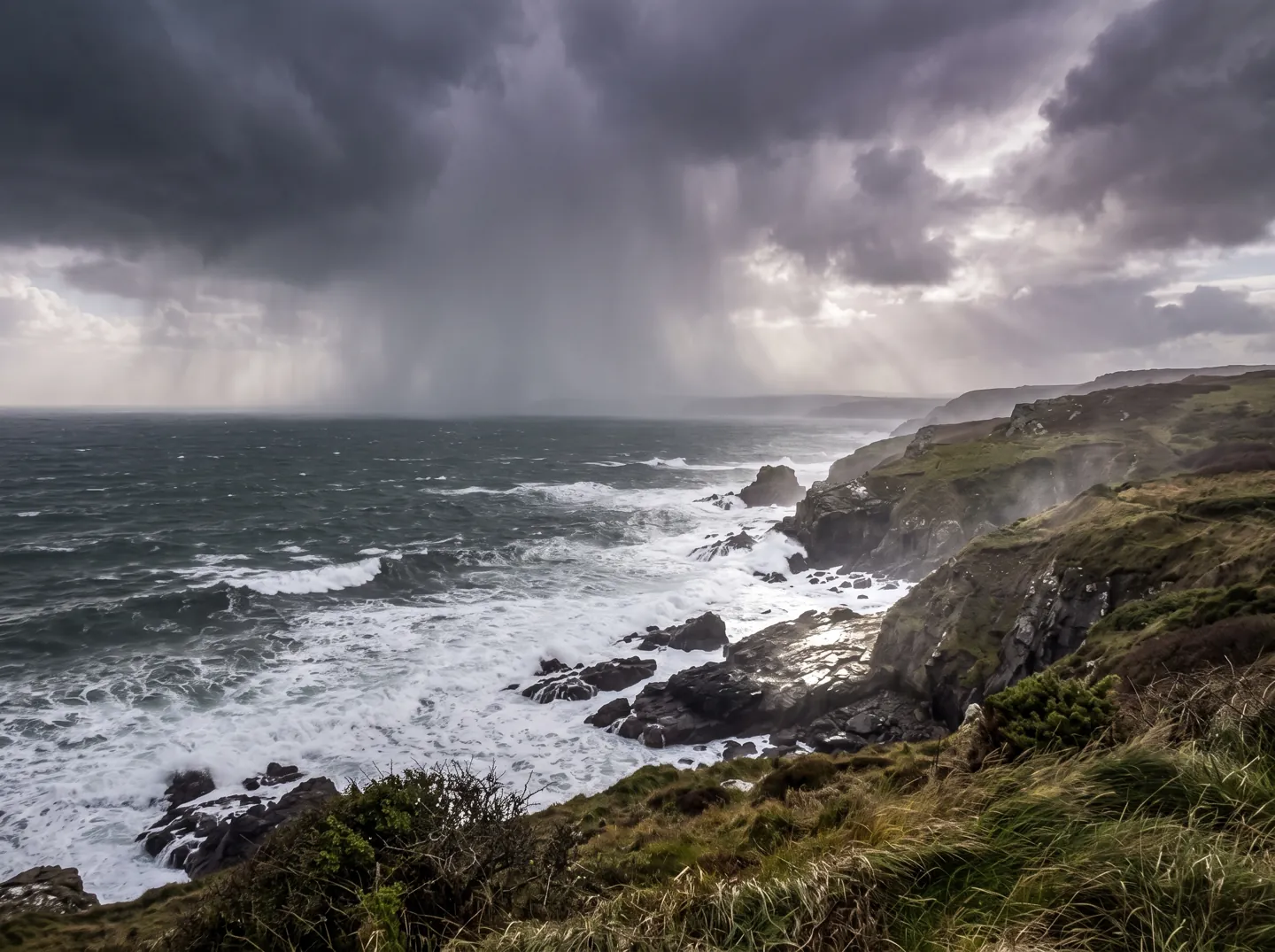 Dark storm clouds and heavy rain sweeping across a windswept British coastline with waves breaking on the shore